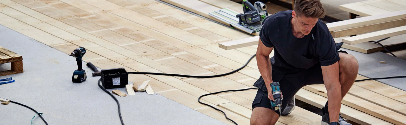 Man in Fristads werkshirt en korte werkbroek die hout bewerkt 