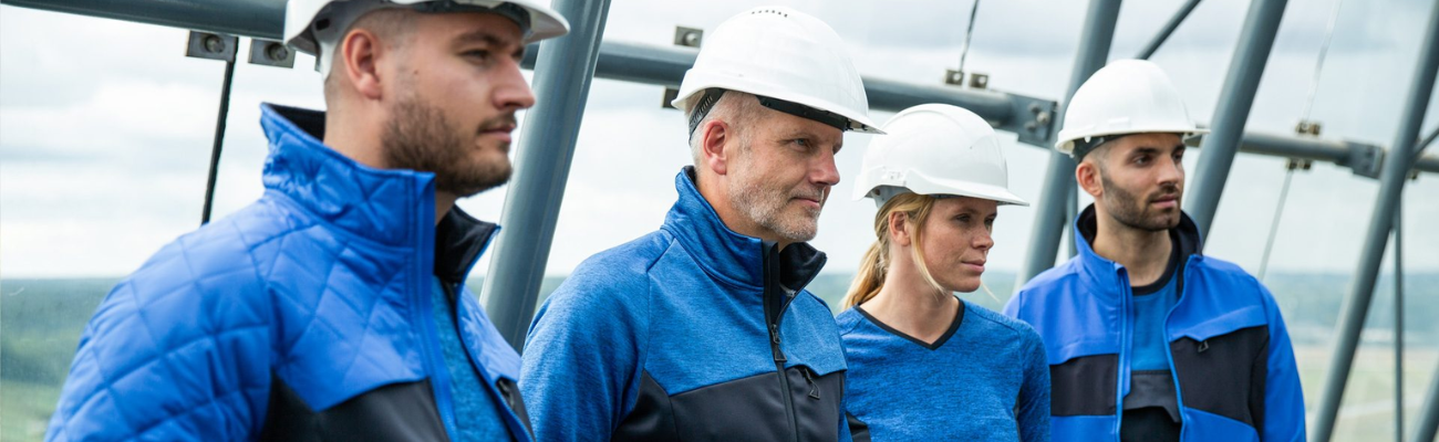 Drie mannen en een vrouw met witte helmen en blauwe werkkleding aan 